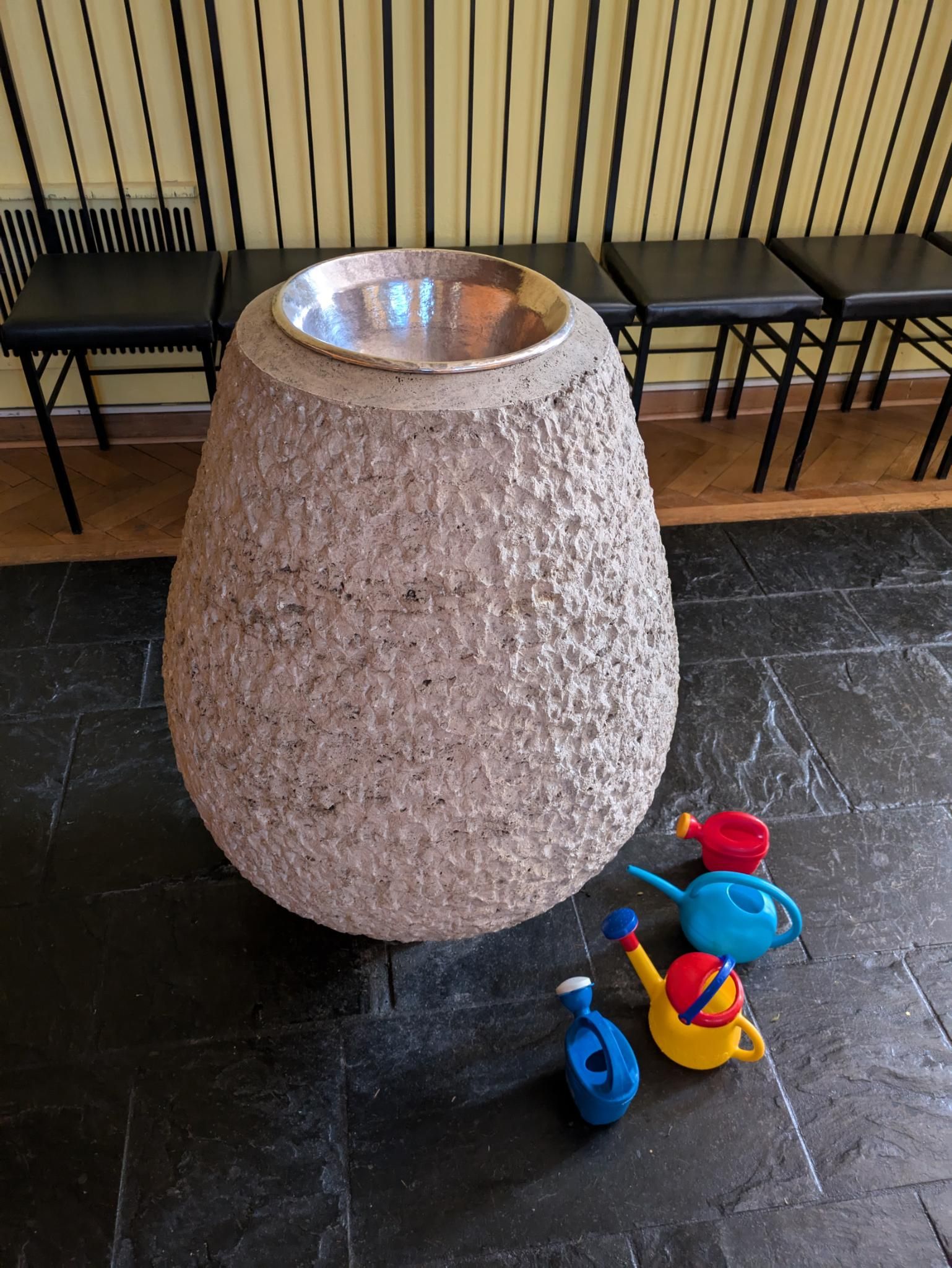 Eiförmiges Taufbecken der Weihnachtskirche mit Kinder-Gießkannen