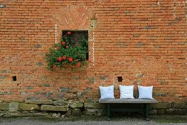 Bild einer Baksteinwand mit Blumen und einer einladenden leeren Bank davor